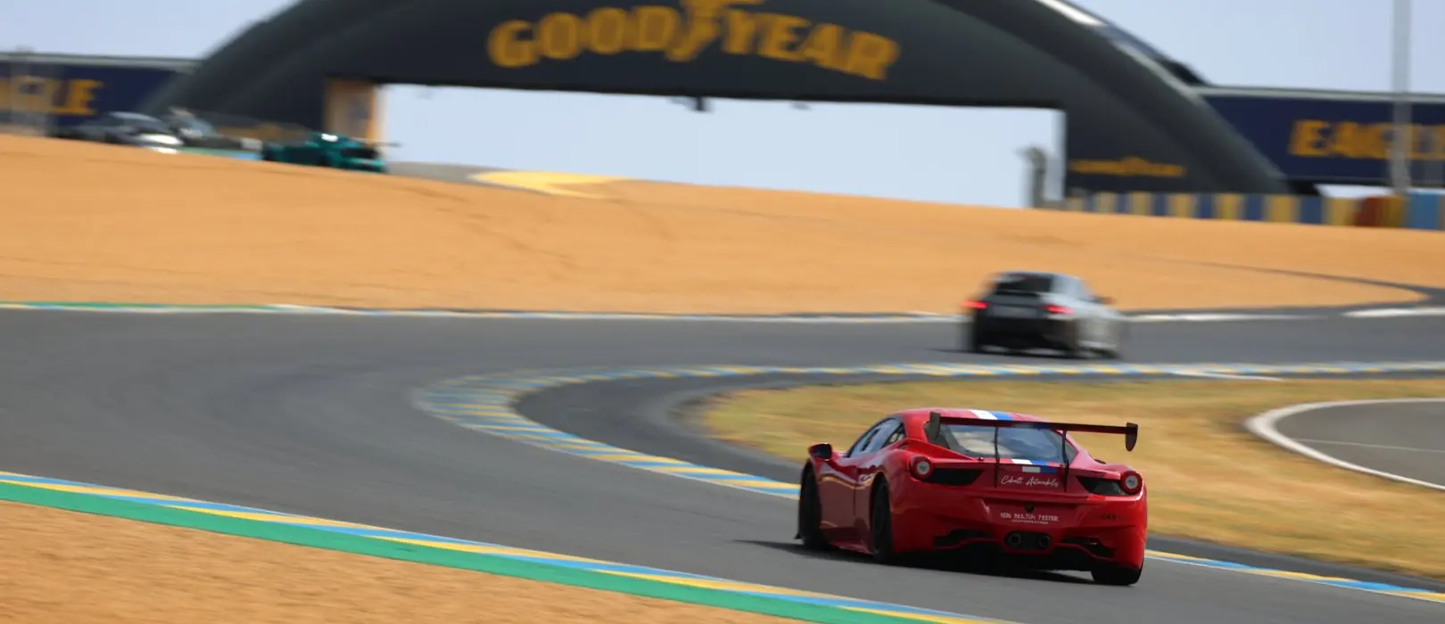 A red car passes under the footbridge at the Le Mans circuit
